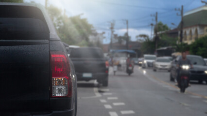 Rear side of pickup car black color. Car parking side of asphalt road. Other cars and motorcycle driving in the city at day time.