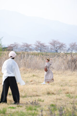 Naklejka premium A woman in a dress is playing with a man in a field. The woman is holding a bag and the man is holding a baseball bat. The scene is peaceful and relaxed