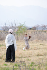 Naklejka premium A woman in a white shirt and black pants is standing in a field watching a woman in a brown shirt and white pants throw a baseball