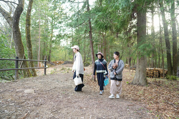 Fototapeta premium Three women are walking through a forest, one of them carrying a baby. The atmosphere is calm and tranquil, with the sound of leaves crunching underfoot