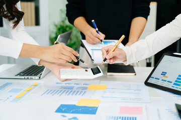 Business documents on office table with smart phone and laptop and three colleagues discussing data in the background in morning light