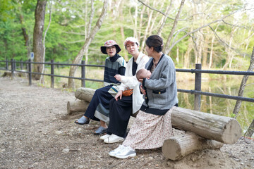 Three women sit on a log in a park, one of them holding a baby. The scene is peaceful and serene, with the women enjoying each other's company and the natural surroundings