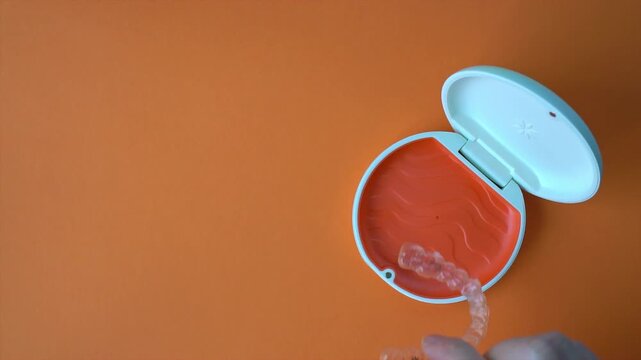 Store an orthodontic aligner in an orange case. Slow motion video. Orange background with copy space.
