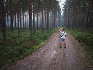 Obraz premium Aerial drone view of a man hiking on a dirt road through a misty pine forest, exploring the wilderness.