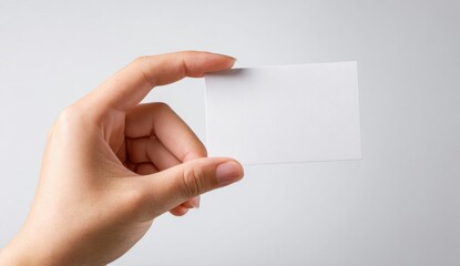 Obraz premium A person holds a small blank rectangular white card between their fingers against a light gray background