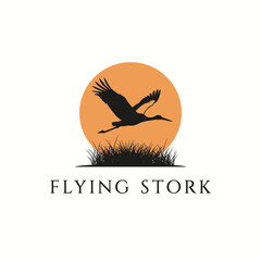 Obraz premium Silhouette of a stork in flight against an orange sunset, with grass and text.