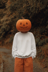 A person wearing a white sweatshirt mockup, orange pants, and a pumpkin head mask for Halloween