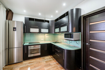 modern kitchen features dark wood cabinetry, a stainless steel refrigerator and oven, and light green countertops. Recessed lighting illuminates the space