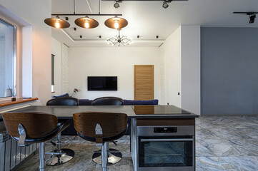 Modern apartment interior featuring a kitchen island with bar stools, a blue sofa, and sleek lighting