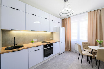 bright, modern kitchen with white cabinets, a wooden countertop, and a sleek black sink. A round white table with tan chairs sits near a window with beige curtains