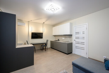 Modern kitchen with gray cabinets, white upper cabinets, a gray table and two chairs. TV on the wall, white door, wood floors