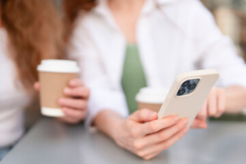 Friends enjoying coffee while browsing on a smartphone at a cafe in the afternoon light during a casual meetup