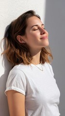 Obraz premium Peaceful young woman enjoying sunlight in front of a smooth white wall 