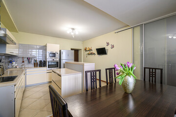 bright kitchen-dining area with a dark wood table, tulips, and modern appliances. The style is clean and comfortable