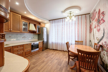 Warm kitchen featuring wood cabinets, a table with chairs, and floral wallpaper. The design is traditional and cozy