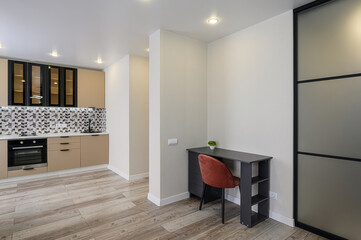 room features light wood floors, a desk with a chair, and a kitchen area with cabinets and appliances