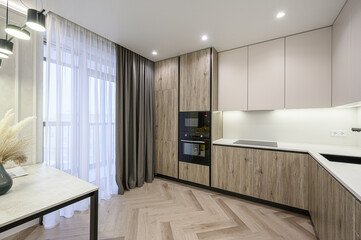 Modern kitchen with wooden cabinets, a white countertop, and herringbone floors. Natural light streams through sheer curtains