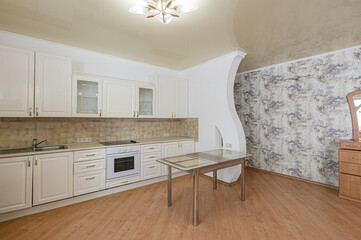 well-lit kitchen features white cabinets, beige tile backsplash, a table, and wood-patterned flooring. The wallpaper with nature prints is behind a wall with an arch