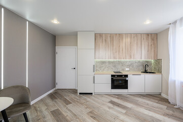 modern kitchen features light wood and white cabinets, a dark sink, and sleek appliances, with a wooden floor and a chair to the side
