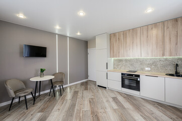 modern kitchen and dining area featuring light wood floors, gray walls, white cabinets with wood accents, a small table with chairs, and integrated LED lighting