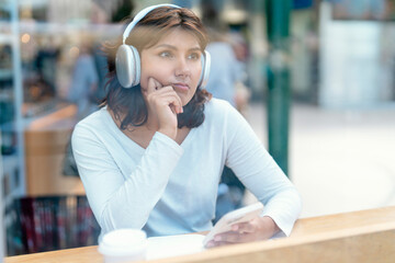 Thoughtful young woman listens to music while sitting in a cafe during the afternoon, enjoying a...
