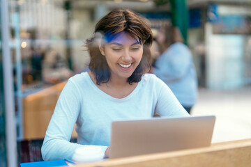 Young woman enjoys working on laptop at modern cafe during afternoon in a busy urban area, surrounded by fellow customers