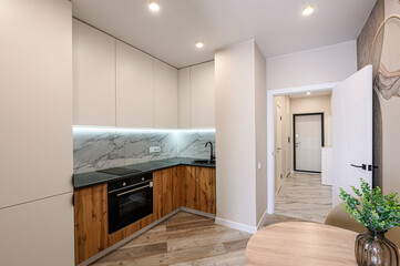 Modern kitchen with sleek cabinets, wood accents, marble backsplash, and a glimpse of a hallway