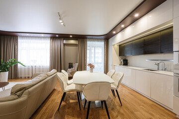 Bright, modern open-concept living space with white furniture, light wood floors, and clean lines. Large windows provide ample light