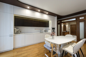 modern kitchen with white cabinets, a dining table, and wooden floors.  Warm lighting