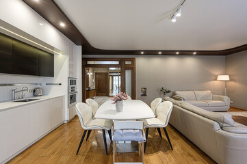 Modern interior with an open kitchen and living area. Features a white dining table, sleek cabinets, wooden floors, and a neutral color palette