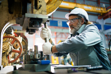 Senior engineer repairing heavy machinery in steel and metal factory.