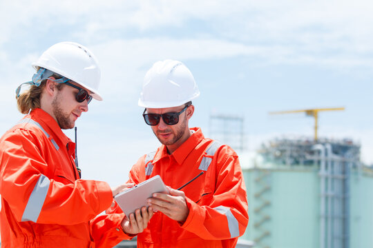 Engineers inspecting oil refinery and gas pipeline system with tablet