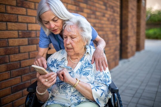 Senior patient in wheelchair showing picture in smartphone to caregiver. - Powered by Adobe