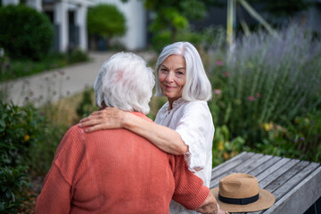 Elderly mother sitting on bench with adult daughter.