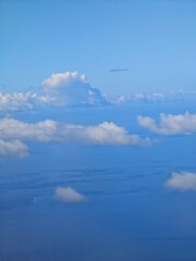 Vast blue sky with fluffy clouds observed during a flight over the ocean in daylight