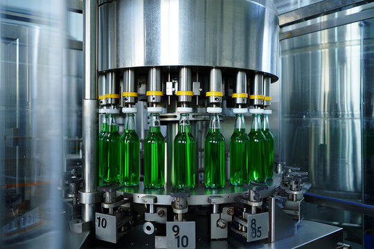 Green liquid filled glass bottles on automated filling machine industrial production - Powered by Adobe