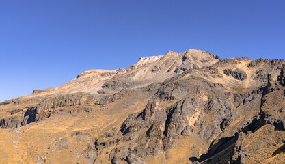 A mountain range with a clear blue sky in the background. The mountain is rocky and barren, with no vegetation visible. The sky is bright and clear. Iztacihuatl popocatepetl volcano mexico,