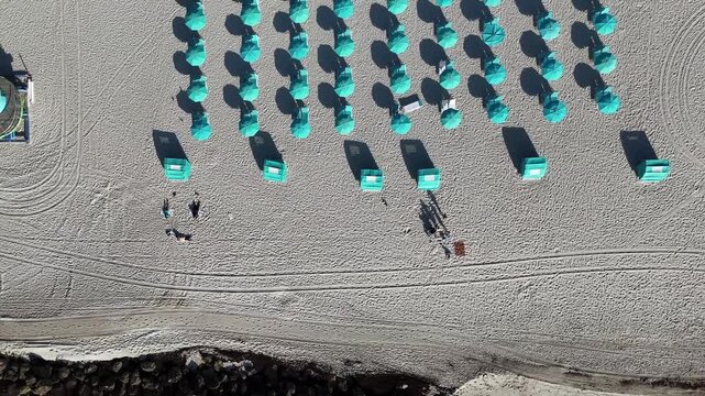 Aerial 4K drone top-down video of turquoise umbrellas and lounge chairs on Miami Beach, Florida, arranged in neat rows with shadows on the sand, creating a geometric and colorful tropical vacation sce