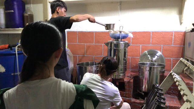 A team of Asian workers is at a small local winery: one is capping bottles, one is scalding bottles, and another is bottling wine.