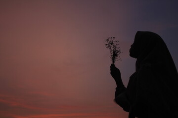 muslimah woman traveling to beach, enjoy the sunset, orange colour, holding flower