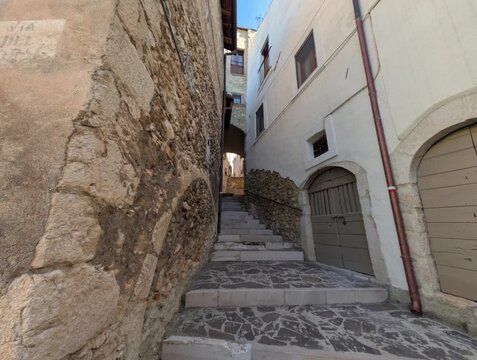 Vicolo in un antico borgo medievale. Le pareti delle case sono costruite in pietra. Nel vicolo ci sono scale e passaggi che si snodano tra le costruzioni.