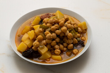 A white plate with chickpeas, potatoes, blood sausage, and chorizo ​​on a veined white marble table