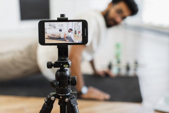 Middle-aged man recording video blog about fitness performing yoga exercise in bright kitchen