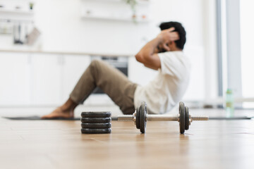 Young adult man indoors doing sit-ups with focus on dumbbell representing fitness theme