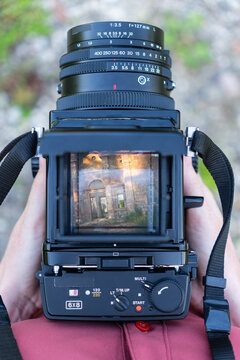 A woman looks through the viewfinder of a vintage medium format camera. In the viewfinder, he sees the antique building on a sunny day