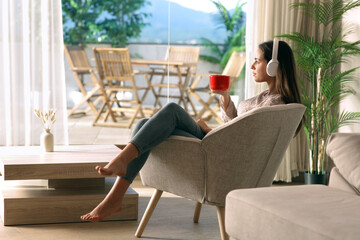 Woman relaxing sitting on armchair drinking coffee listening aud