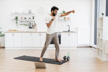 Man in 30s practicing boxing exercises in spacious kitchen on yoga mat, showing fitness.