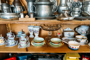 A collection of vintage porcelain teacups, saucers, and antique pewterware arranged on wooden...
