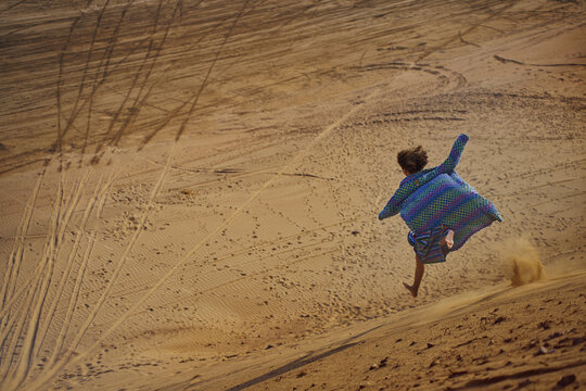 Man in patchwork caftan running barefoot in sandy desert