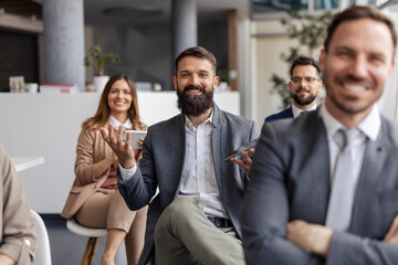 Fototapeta premium Bearded businessman sitting in audience and asking questions on seminar while smiling at camera.